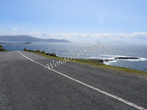Route côtière à Keel, Irlande, avec vue sur l'océan et les collines en arrière-plan.