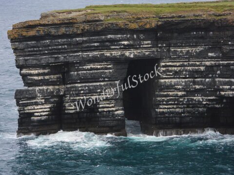 Rocher aux strates visibles à Loop Head, Irlande, avec des vagues s'écrasant contre la base.