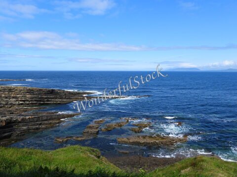 Rochers côtiers à Mullaghmore Head, Irlande, avec des vagues s'écrasant sur les rochers et un ciel bleu partiellement nuageux.