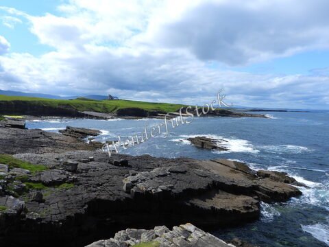 Rochers côtiers à Mullaghmore Head, Irlande, avec des vagues qui se brisent et une colline verdoyante en arrière-plan.