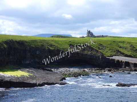 Falaises verdoyantes et roches au bord de l'eau, avec un château en arrière-plan à Mullaghmore Head, Irlande.