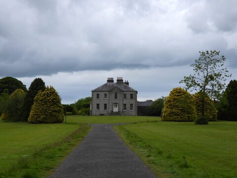 Maison entourée de grands arbres, située à The Dark Hedges, Irlande. Ciel nuageux et allée menant à l'entrée principale.
