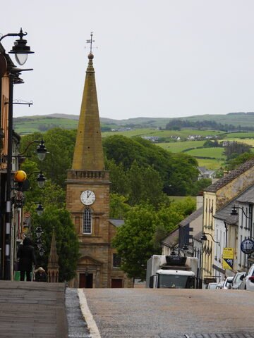 Église avec une flèche sur une rue de Ballycastle, Irlande, entourée de collines verdoyantes et de maisons colorées.
