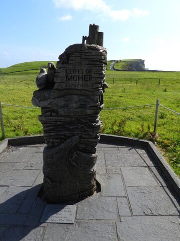 Sculpture en bois aux Cliffs of Moher, Irlande, avec une vue sur la verdure environnante et le bord de la falaise au loin.