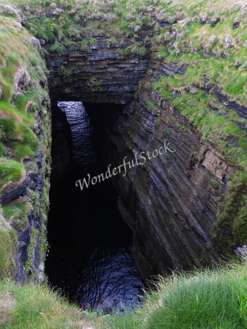 Falaise escarpée avec un gouffre sombre à Downpatrick Head, Irlande, entourée d'herbe verte et de parois rocheuses.