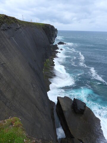 Falaises abruptes au Loop Head, en Irlande, avec des vagues s'écrasant contre la roche et un ciel nuageux en arrière-plan.