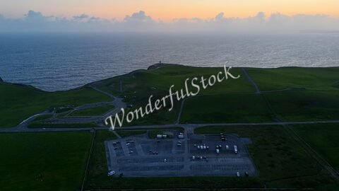Vue aérienne des falaises de Moher en Irlande, avec des champs verdoyants et un parking visible près de l'océan.