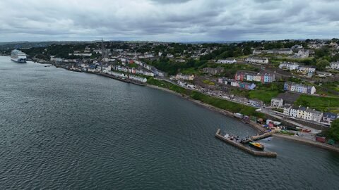 Vue aérienne de Cobh, en Irlande, montrant des maisons colorées le long de la côte et un bateau de croisière dans la baie.