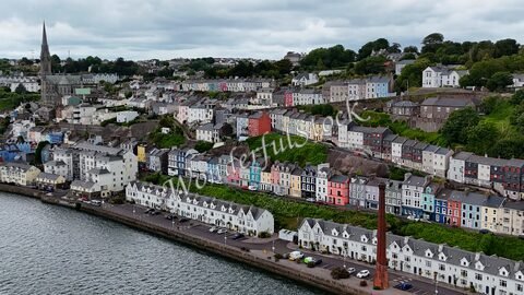 Maisons colorées surplombant le port à Cobh, Irlande, avec une église en arrière-plan et un ciel nuageux.