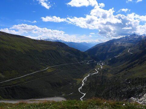 Vue panoramique du glacier du Rhône en Suisse, avec des montagnes, des vallées verdoyantes et des routes sinueuses.