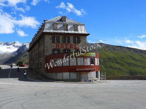 Hôtel avec une façade en pierre et un toit en métal, situé au Belvédère, Suisse, avec des montagnes et un glacier en arrière-plan.