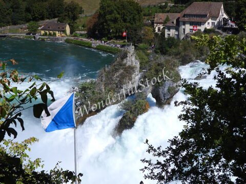 Chutes d'eau majestueuses aux Chutes du Rhin, Suisse, avec des drapeaux et des bâtiments en arrière-plan.