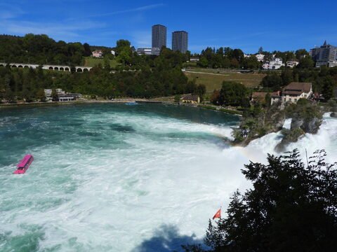 Chutes du Rhin en Suisse, avec des eaux tumultueuses et un bateau rose naviguant près des rives.