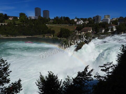 Chutes d'eau à Neuhausen am Rheinfall, Suisse, avec un bateau de croisière et un arc-en-ciel au-dessus des eaux tumultueuses.