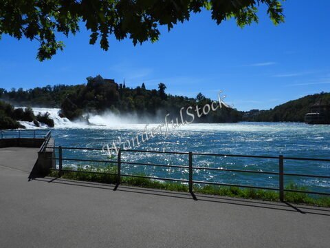 Chutes d'eau aux Chutes du Rhin, Suisse, avec un paysage verdoyant et un bâtiment visible sur la colline.
