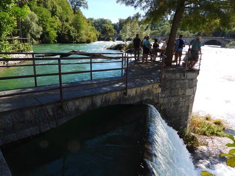 Chutes du Rhin, Suisse, avec un pont en pierre et des visiteurs admirant le paysage au bord de la rivière.