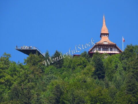 Un bâtiment avec un toit en pointe surplombe une plateforme d'observation à Interlaken, Suisse, entouré de verdure.
