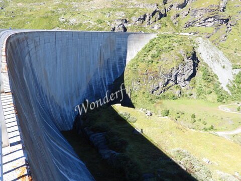 Barrage surplombant une vallée verdoyante à Moiry, en Suisse, avec des montagnes en arrière-plan et un ciel dégagé.