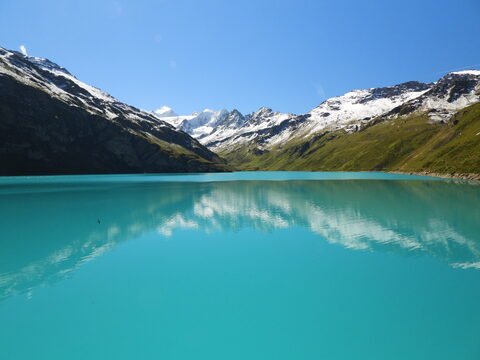 Lac de Moiry en Suisse, avec des montagnes enneigées en arrière-plan et des reflets sur l'eau turquoise.