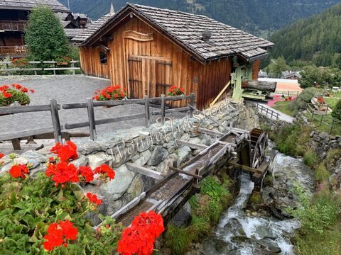 Maison en bois avec une roue à eau et des géraniums rouges à Grimentz, Suisse.