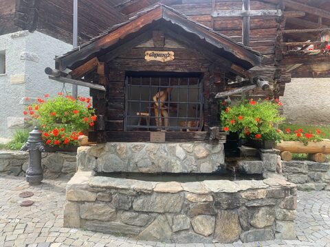 Fontaine en bois ornée de fleurs rouges, située à Grimentz, Suisse.