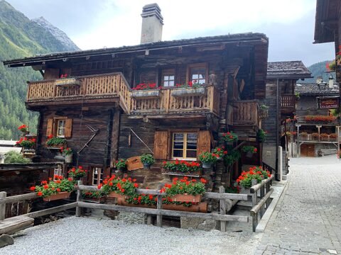 Maison en bois avec balcons fleuris à Grimentz, Suisse, entourée de montagnes verdoyantes.