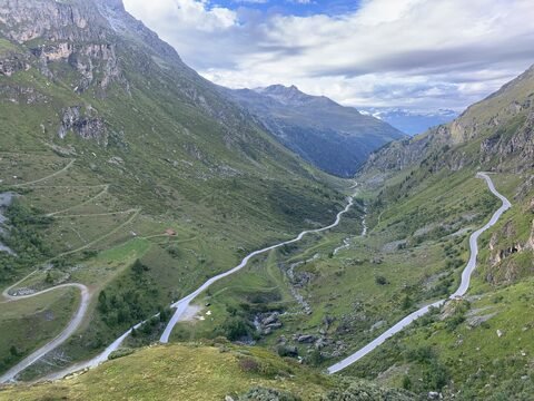 Vallée verdoyante avec des routes sinueuses à Grimentz, Suisse, entourée de montagnes et de nuages.