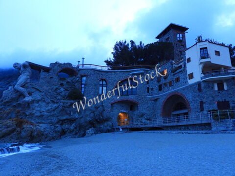 Bâtiment en pierre sur une plage à Monterosso, Italie, avec une sculpture humaine et des fenêtres arrondies.