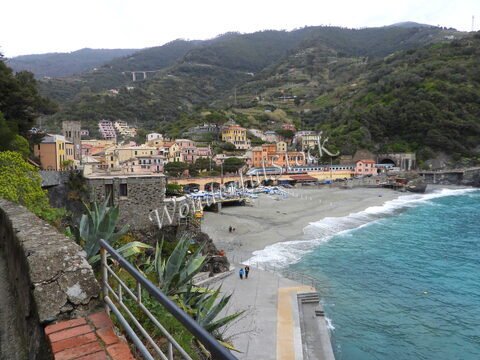 Plage de Monterosso en Italie, avec des bâtiments colorés et des collines verdoyantes en arrière-plan.