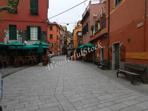 Rue pavée à Monterosso, Italie, avec des parasols verts, des bancs en bois et des bâtiments colorés.