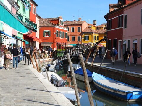 Des canaux bordés de maisons colorées à Murano, Italie, avec des promeneurs et des bateaux amarrés.