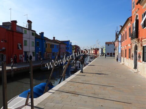 Canaux bordés de maisons colorées à Murano, Italie, avec des personnes et des bateaux amarrés le long de la promenade.