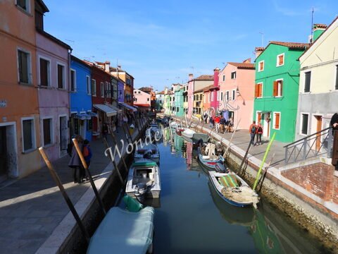 Canaux bordés de maisons colorées à Murano, Italie, avec des bateaux amarrés et des passants sur les quais.
