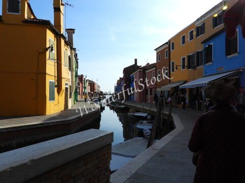 Canaux bordés de maisons colorées à Murano, Italie, avec des personnes se promenant le long de la rive.