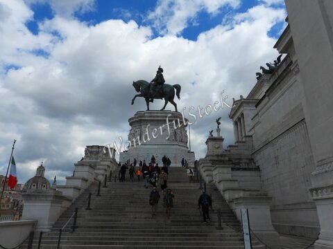 Statue équestre sur un socle à Rome, Italie, avec des visiteurs montant les marches et un ciel nuageux en arrière-plan.