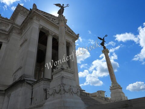 Colonnes et statues au sommet d'un édifice à Rome, Italie, sous un ciel bleu parsemé de nuages.