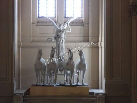 Statue d'une figure ailée entourée de quatre chevaux à Rome, Italie, dans un espace architectural éclairé par des fenêtres.