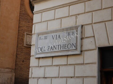 Plaque de rue indiquant "Via del Pantheon" à Rome, Italie, avec un mur en pierre et des éléments architecturaux en arrière-plan.