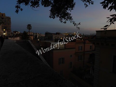 Vue de bâtiments et d'une rue à Rome, Italie, avec un ciel crépusculaire et des palmiers en arrière-plan.