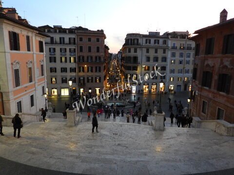 Vue des escaliers avec des personnes et des bâtiments à Rome, Italie, illuminés par des lampadaires au crépuscule.
