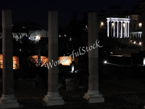 Colonnades éclairées du Forum romain à Rome, Italie, avec des bâtiments historiques en arrière-plan.