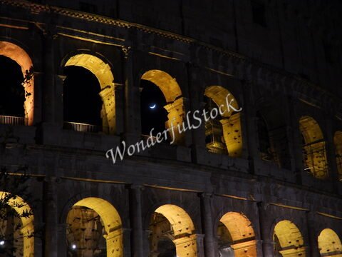 Colisée illuminé à Rome, Italie, avec un croissant de lune visible dans le ciel nocturne.