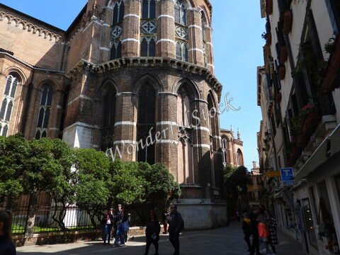 Édifice ancien avec des murs en briques et des fenêtres gothiques, dans une rue de Venise, Italie, entouré de verdure et de passants.