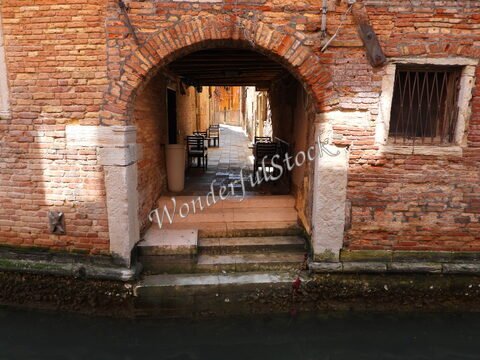Passage avec des murs en briques et des tables à Venise, Italie, donnant sur un canal.