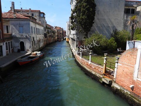 Un canal à Venise, Italie, avec des bâtiments historiques, un bateau orange et des arbres verdoyants le long des rives.