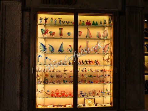 Vitrine de verre présentant des objets en verre coloré à Venise, Italie, avec des formes variées et des éclairages doux.