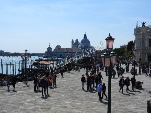 Promenade animée avec des visiteurs et des gondoles à Venise, Italie, devant des bâtiments historiques et le canal.