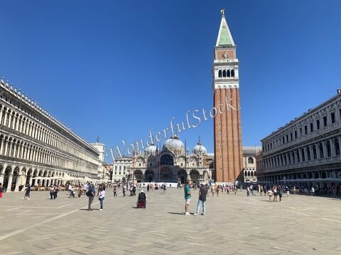 Place Saint-Marc à Venise, Italie, avec le campanile et la basilique, entourée de visiteurs sous un ciel bleu.