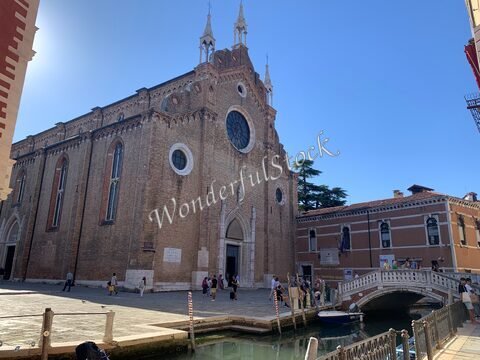 Église en briques avec une grande rosace, située à Venise, Italie, entourée de canaux et de bâtiments historiques.