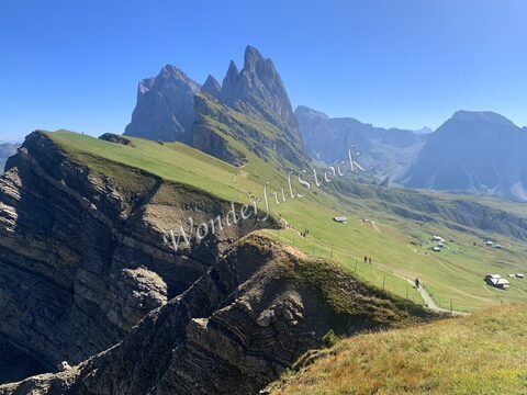 Montagnes et prairies à Seceda, Italie, avec des sentiers et des randonneurs sur un paysage alpin sous un ciel dégagé.